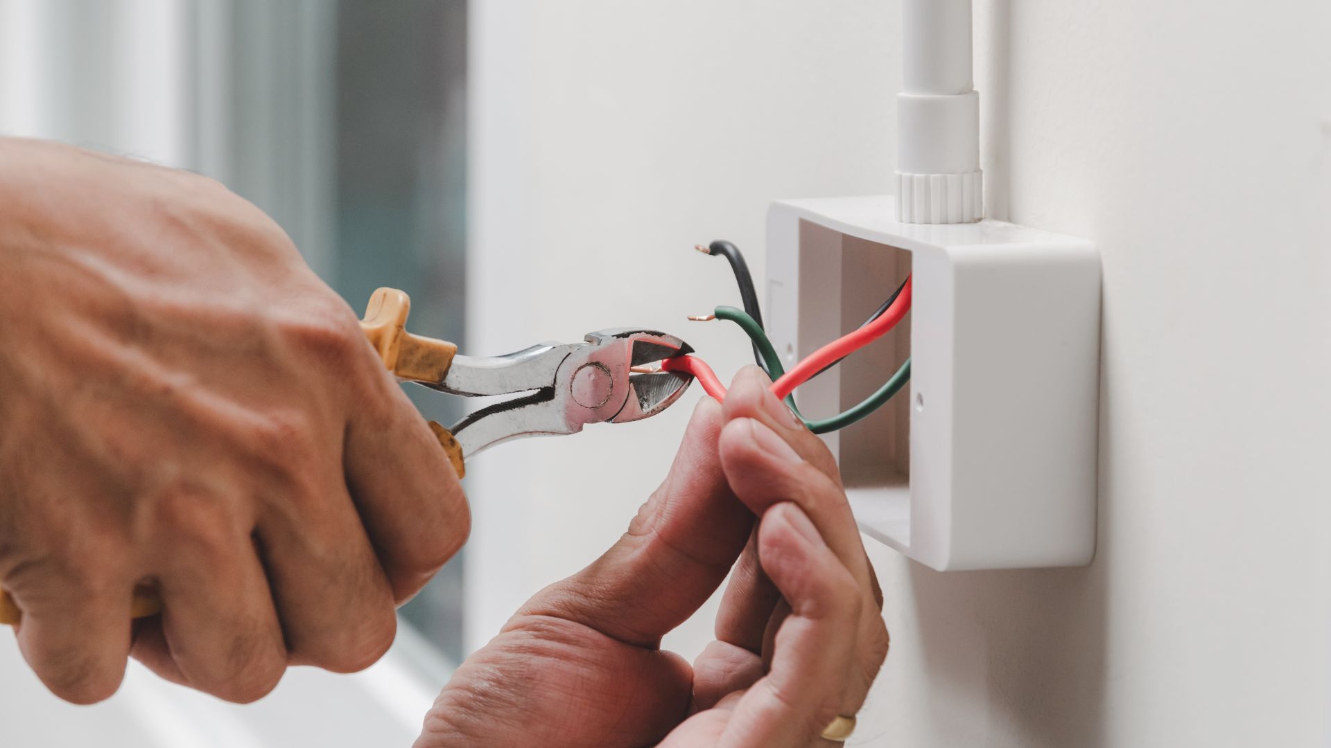 A pair of hands holding a pair of pliers to a light switch